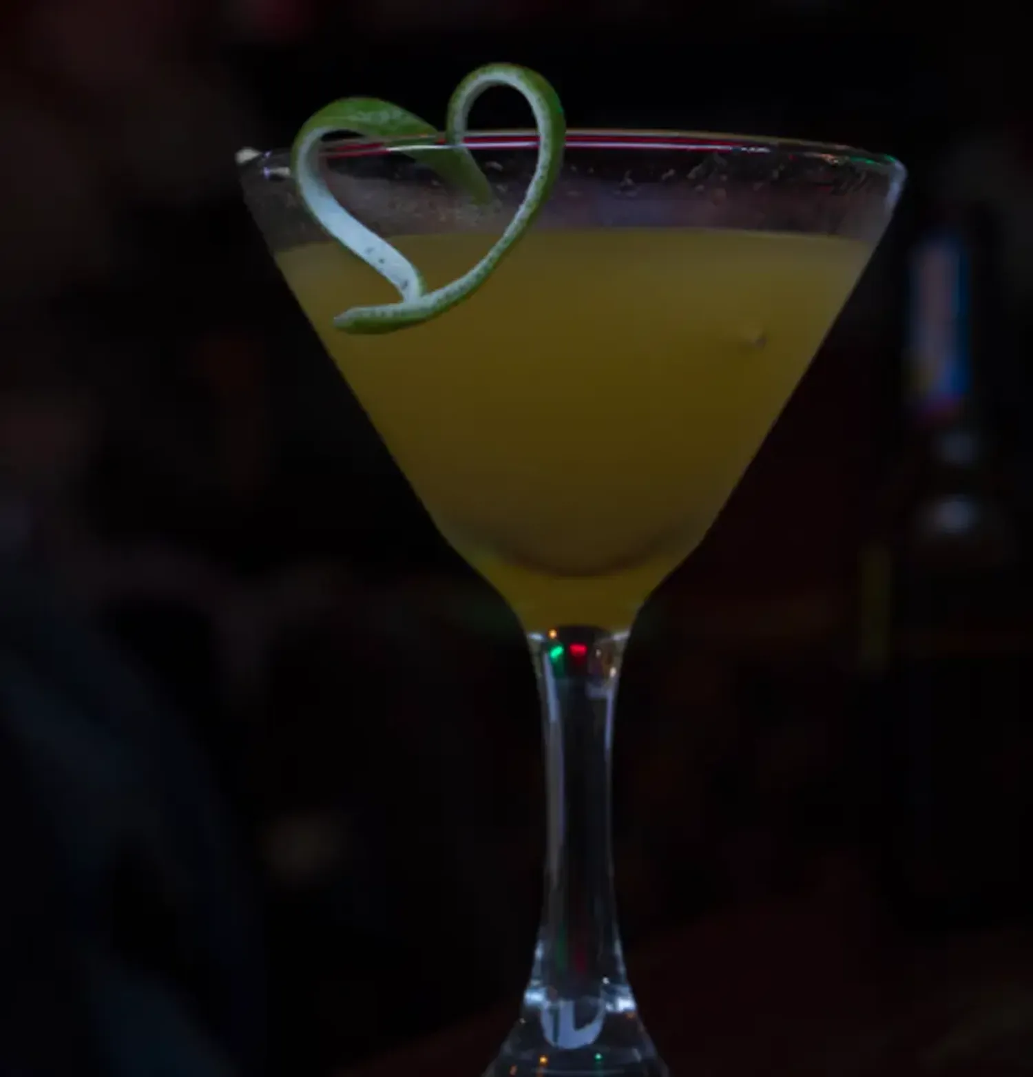Cocktail in a martini glass decorated with a heart-shaped lemon peel strip