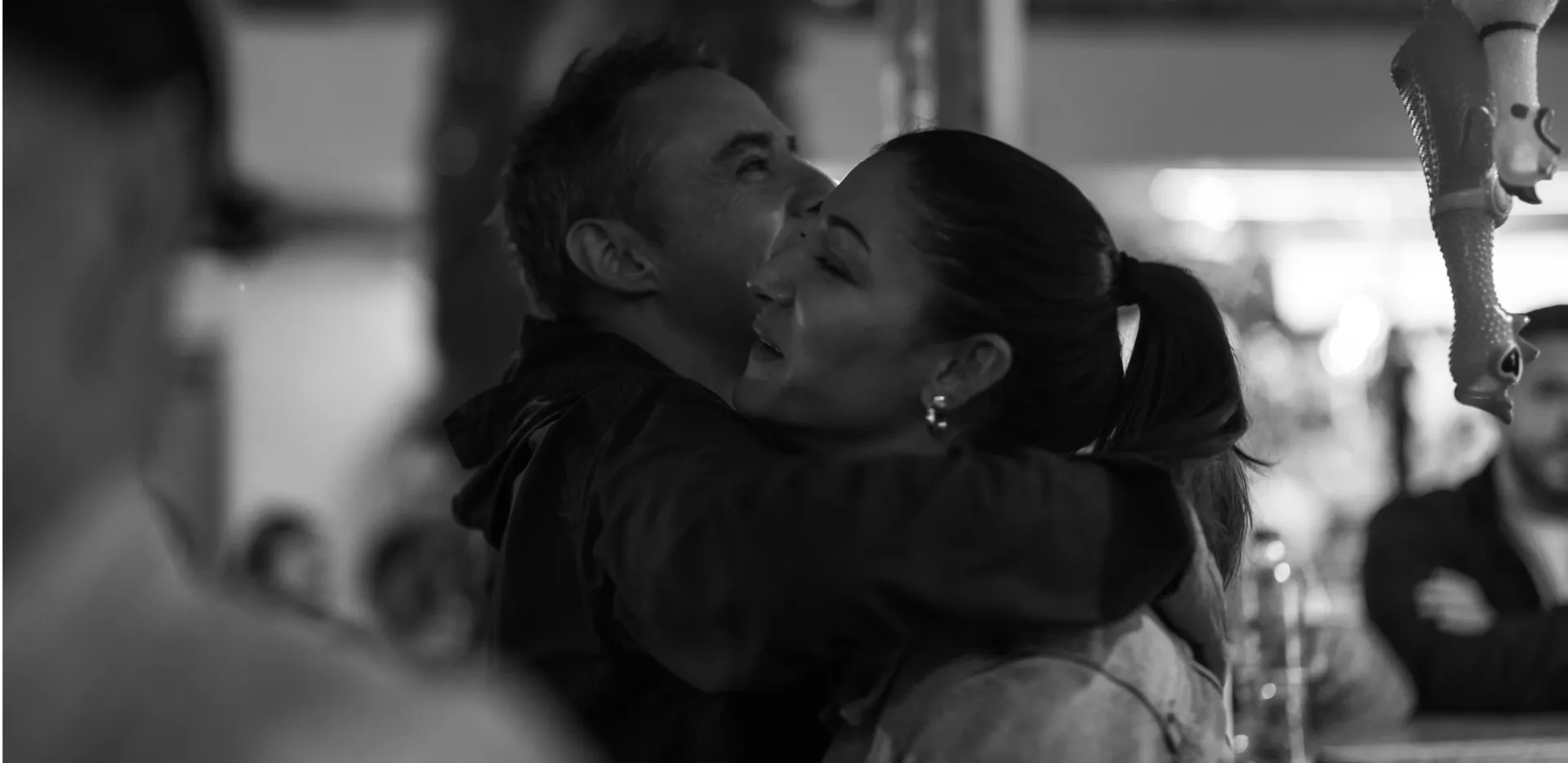 A smiling man and woman hugging each other warmly in a candid, black and white photograph.
