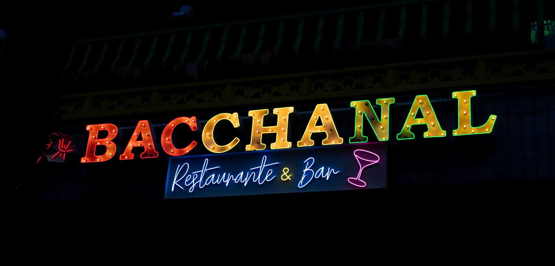 A vibrant and colorful marquee and neon sign for 'Bacchanal Restaurante & Bar' glowing at night.