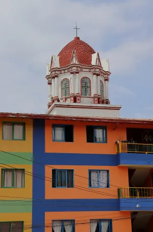 The red-tiled dome of a church tower rises behind a brightly colored building painted in horizontal stripes of orange and blue